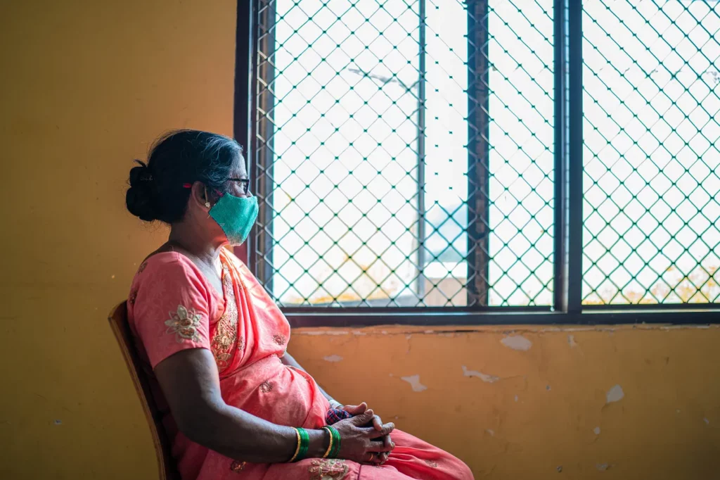 A woman in a mask looks out of a hospital window.