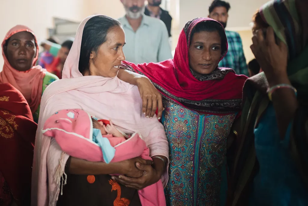 A group of three Indian women talk to each other while one of them holds a baby.