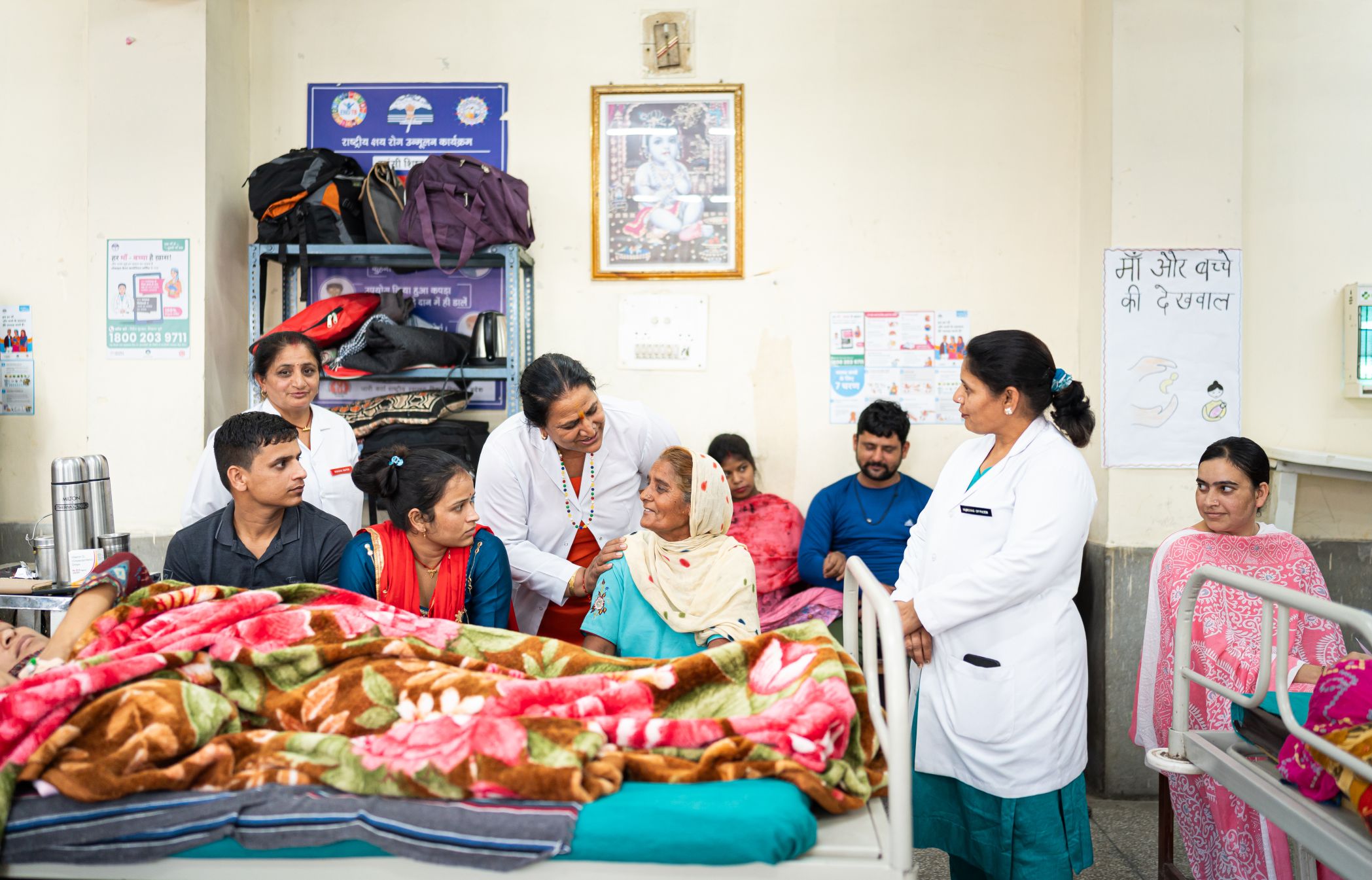 A nurse shares a light moment with a caregiver in a hospital ward, while other caregivers look on.