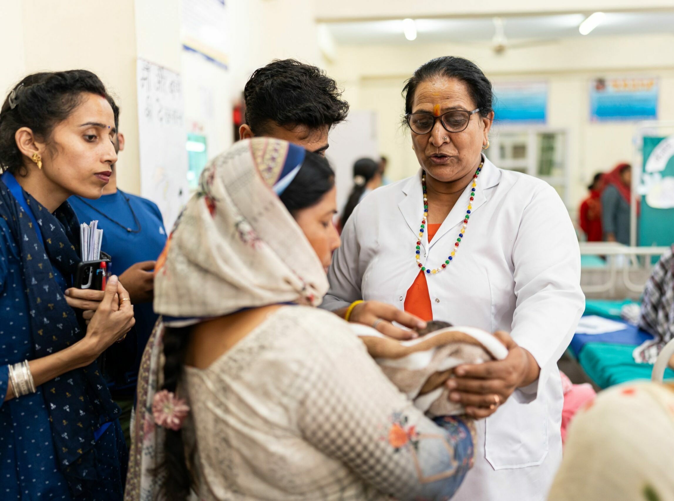 A nurse checks a baby while her mother holds her and other caregivers look on