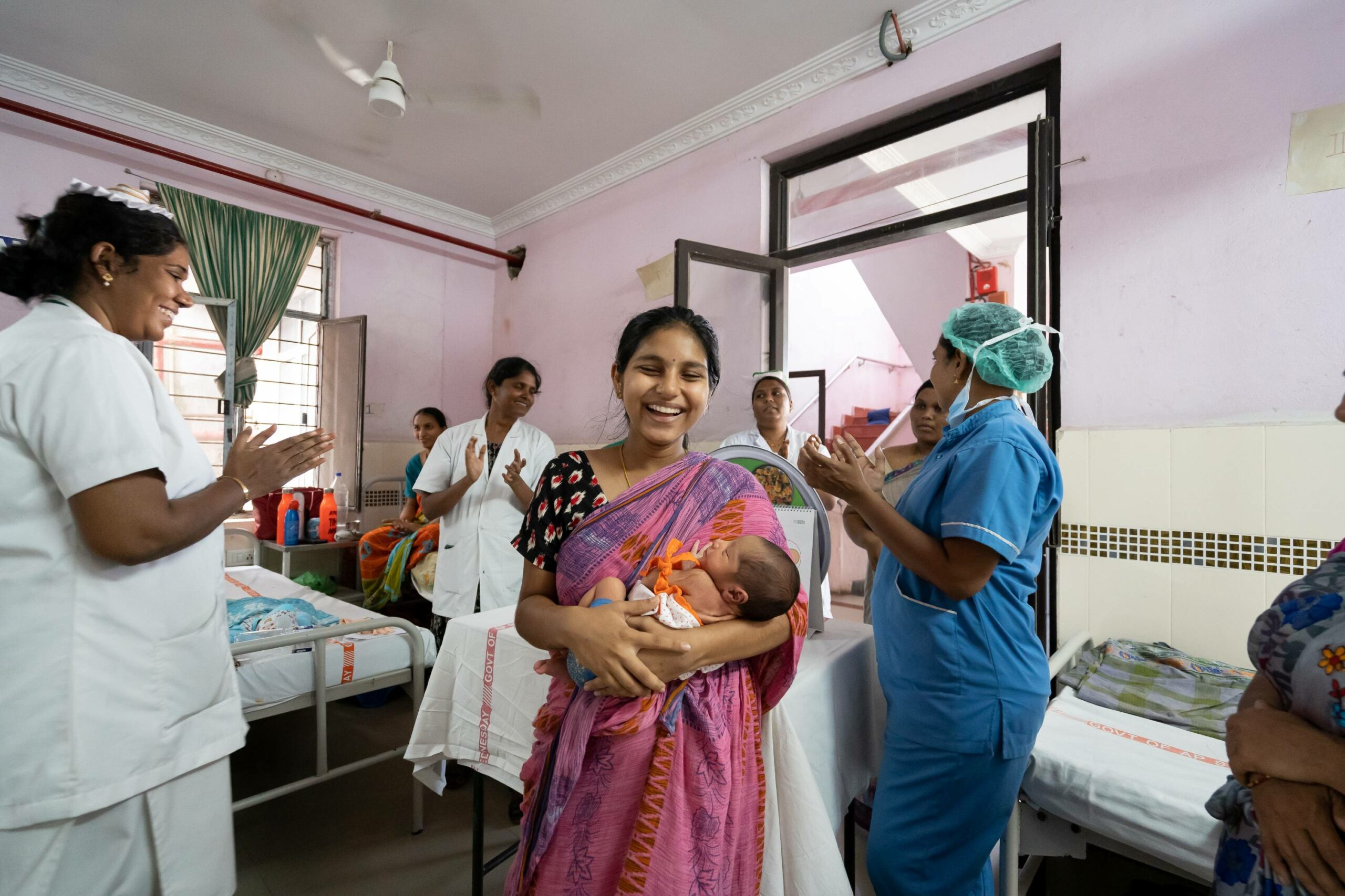 Surrounded by clapping nurses, a mother smiles as she holds her newborn baby in a hospital ward in Andhra Pradesh.