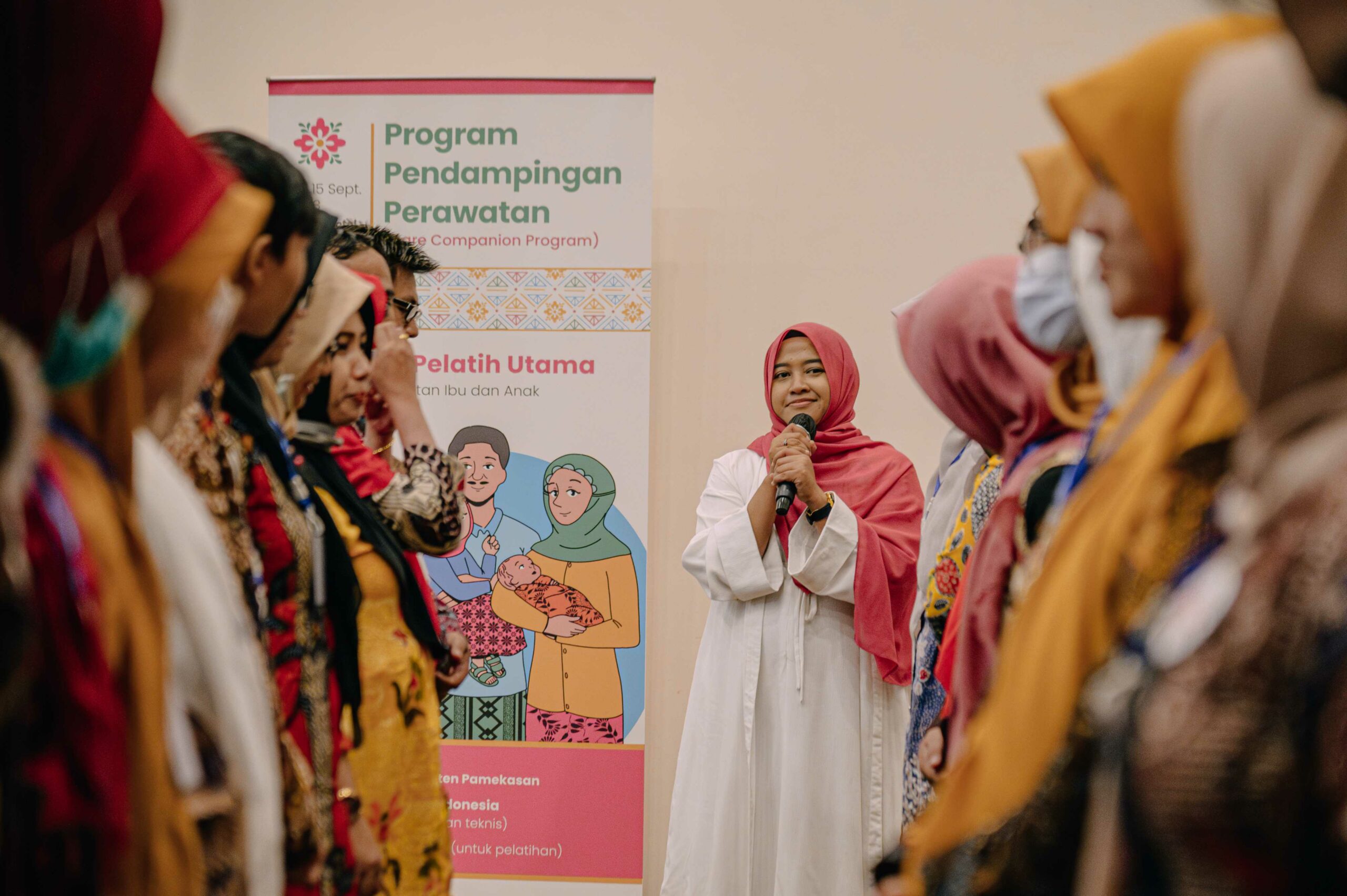 A master trainer stands in the center in focus with nurses lined up on either side of her during a group activity during a Noora Health training of trainers session in Pamekasan, Indonesia