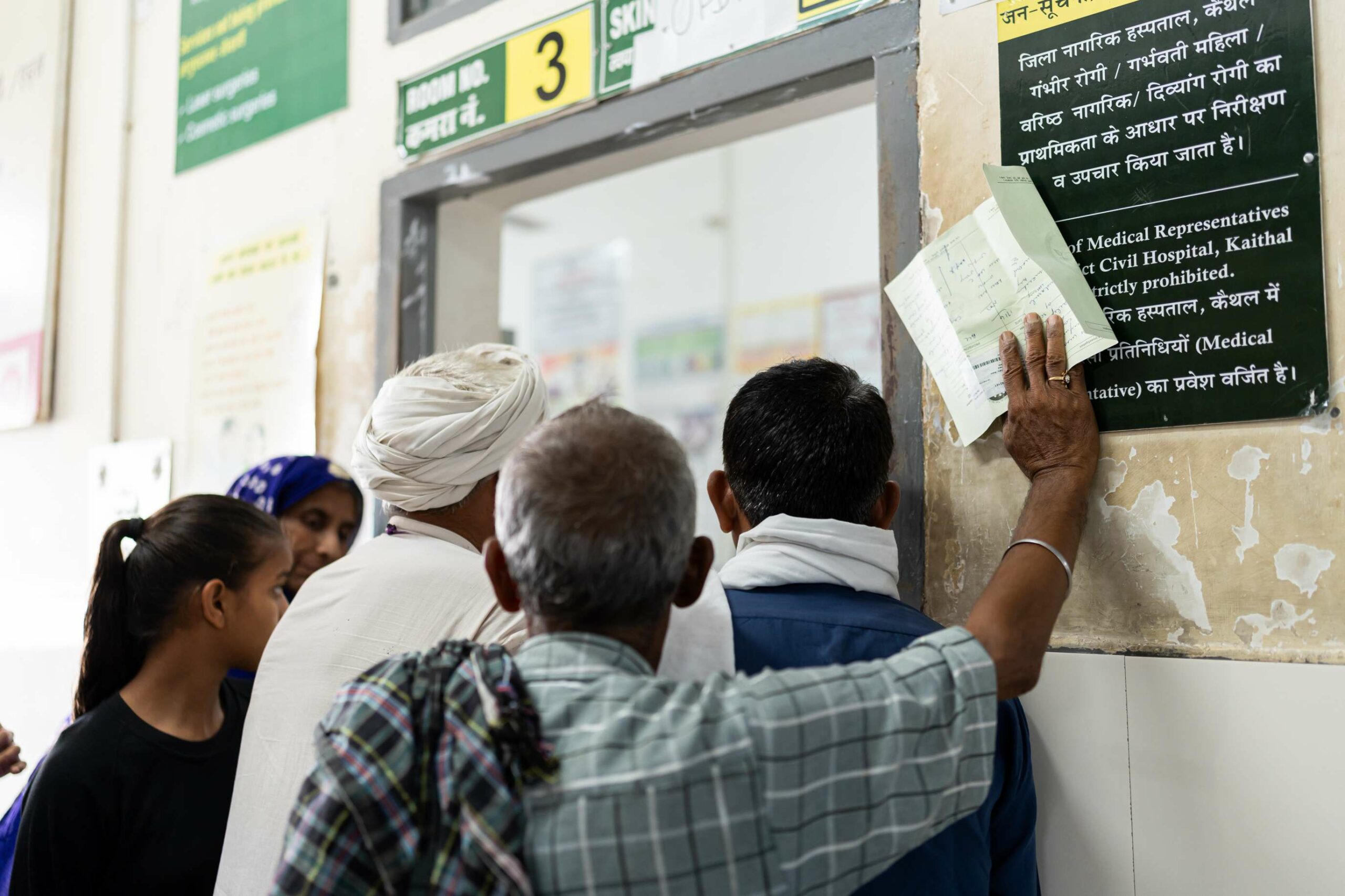 Back view of three men and two women standing at a counter in a hospital in Haryana.