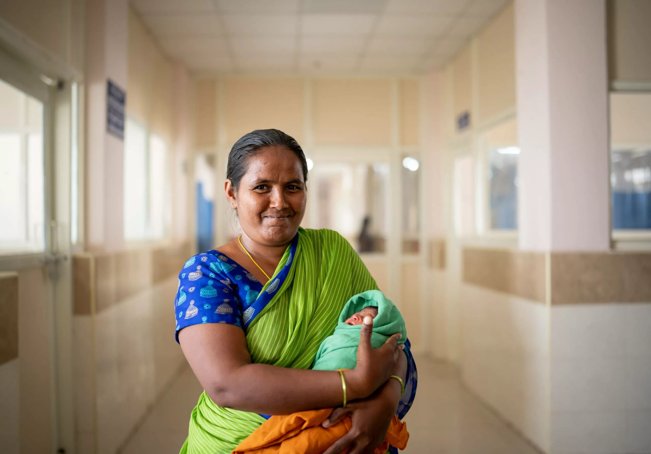 A smiling caregiver holds her newborn baby in the corridor of a hospital in Andhra Pradesh, India.