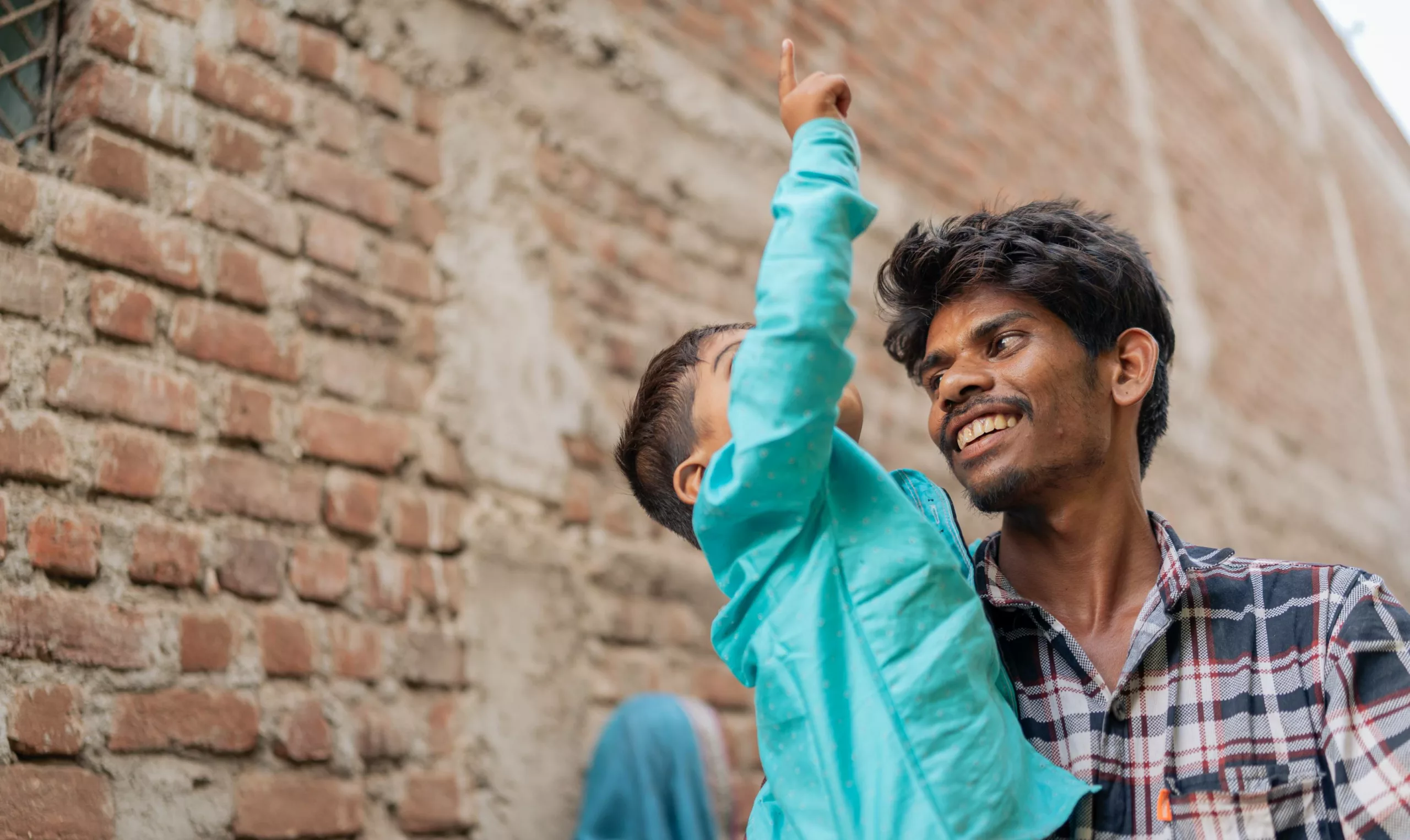 A close up of a smiling father carrying his young son, who is pointing up.