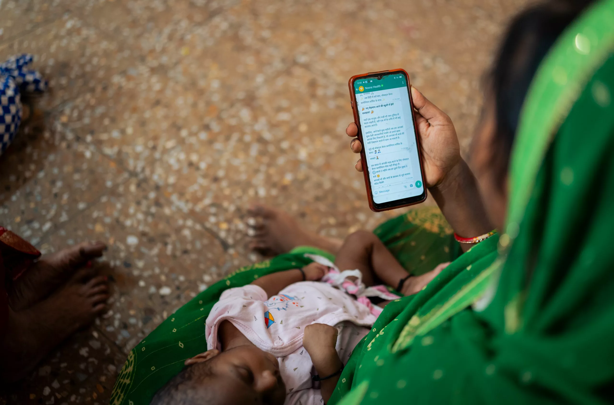 A top shot of a mother accessing Noora Health's postnatal care mobile health service while holding her newborn baby.