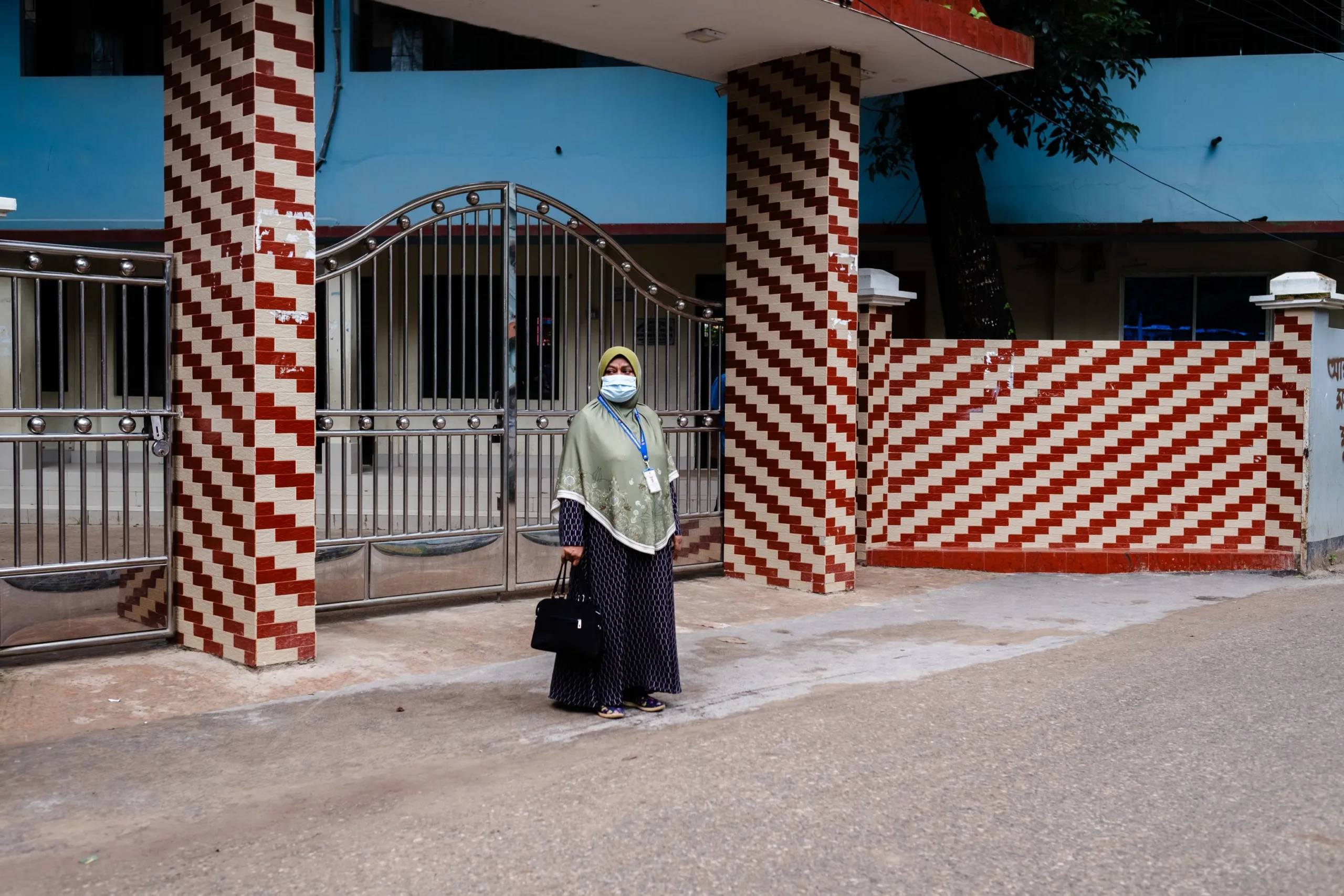 Mahmuda stands outside her house, waiting for a rickshaw to arrive to take her to work.