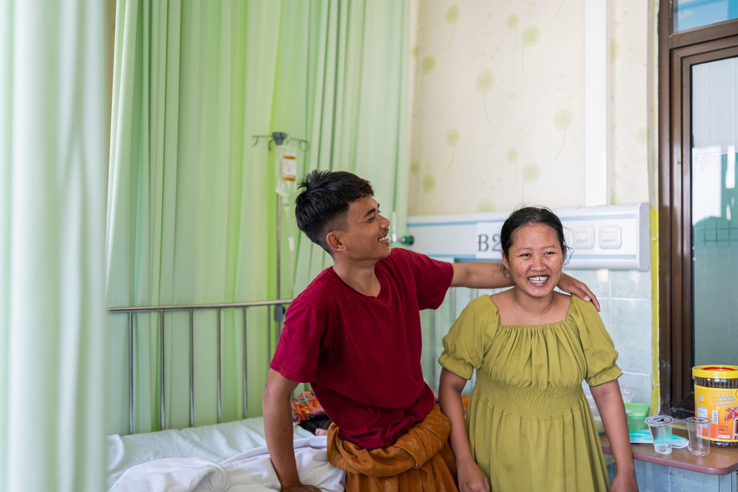 A man and a woman hug each other sideways and laugh in a hospital ward in Pamekasan, Indonesia.