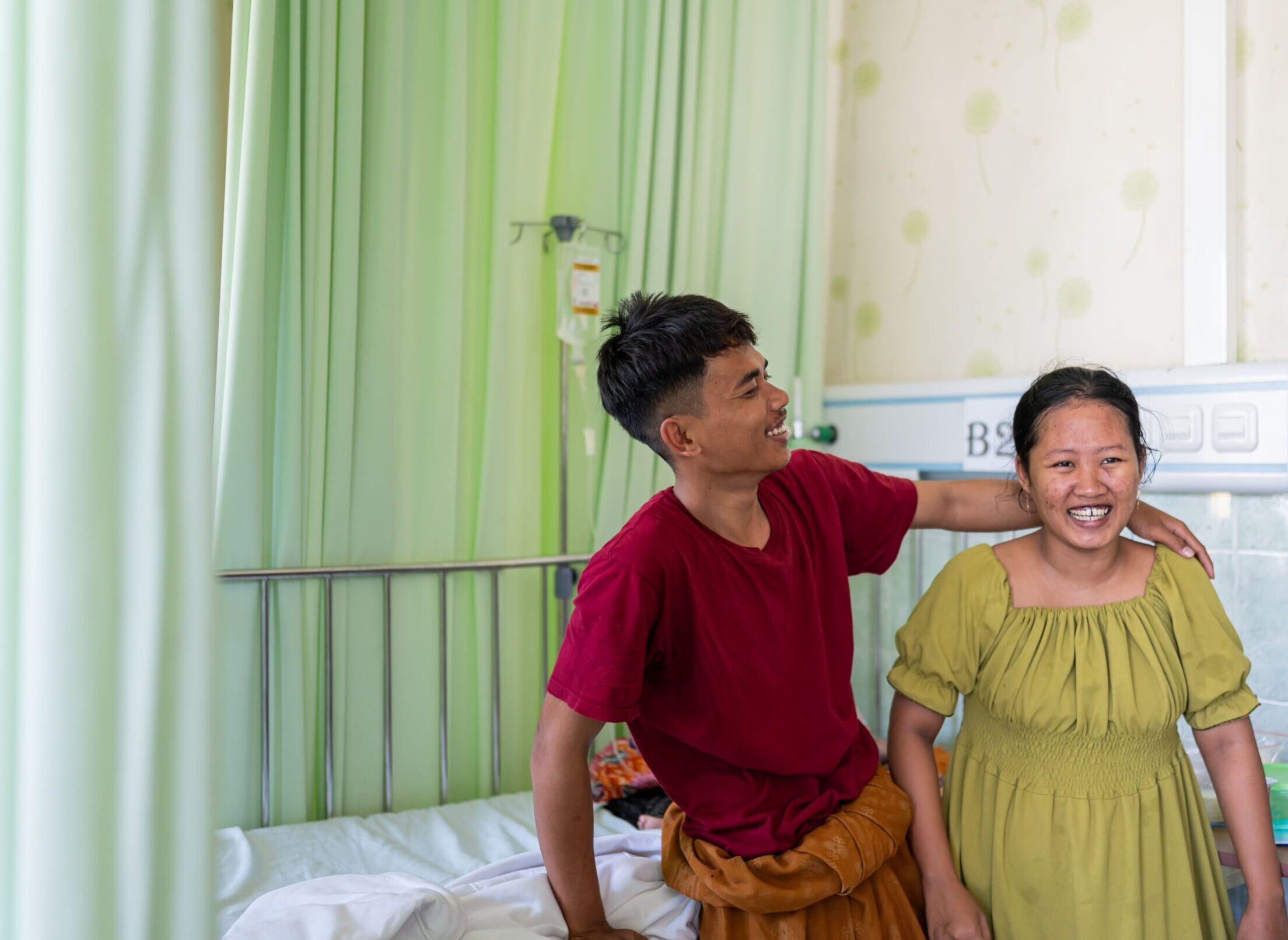 A man and a woman hug each other sideways and laugh in a hospital ward in Pamekasan, Indonesia.