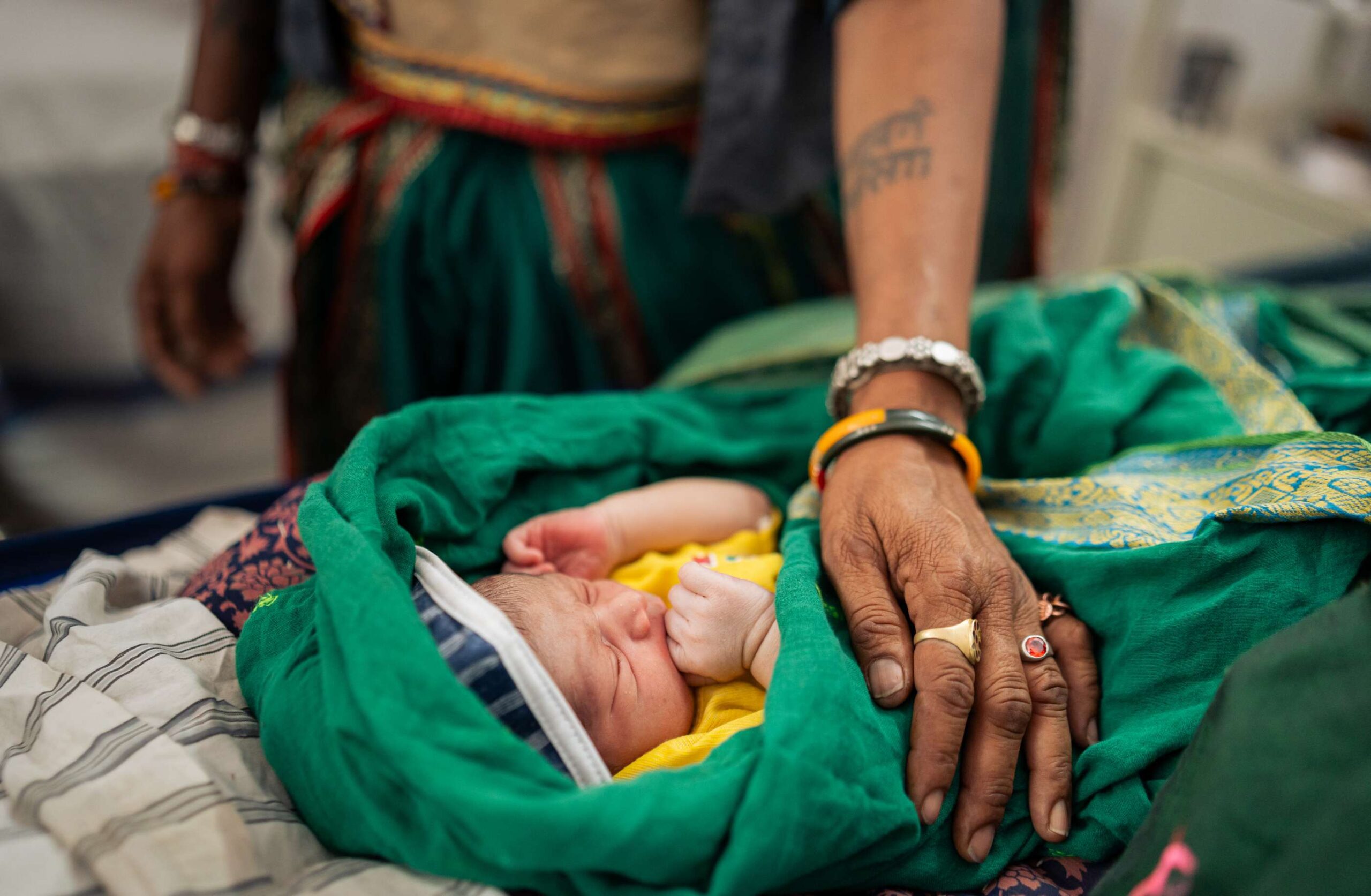 A caregiver places their hand on a newborn baby.