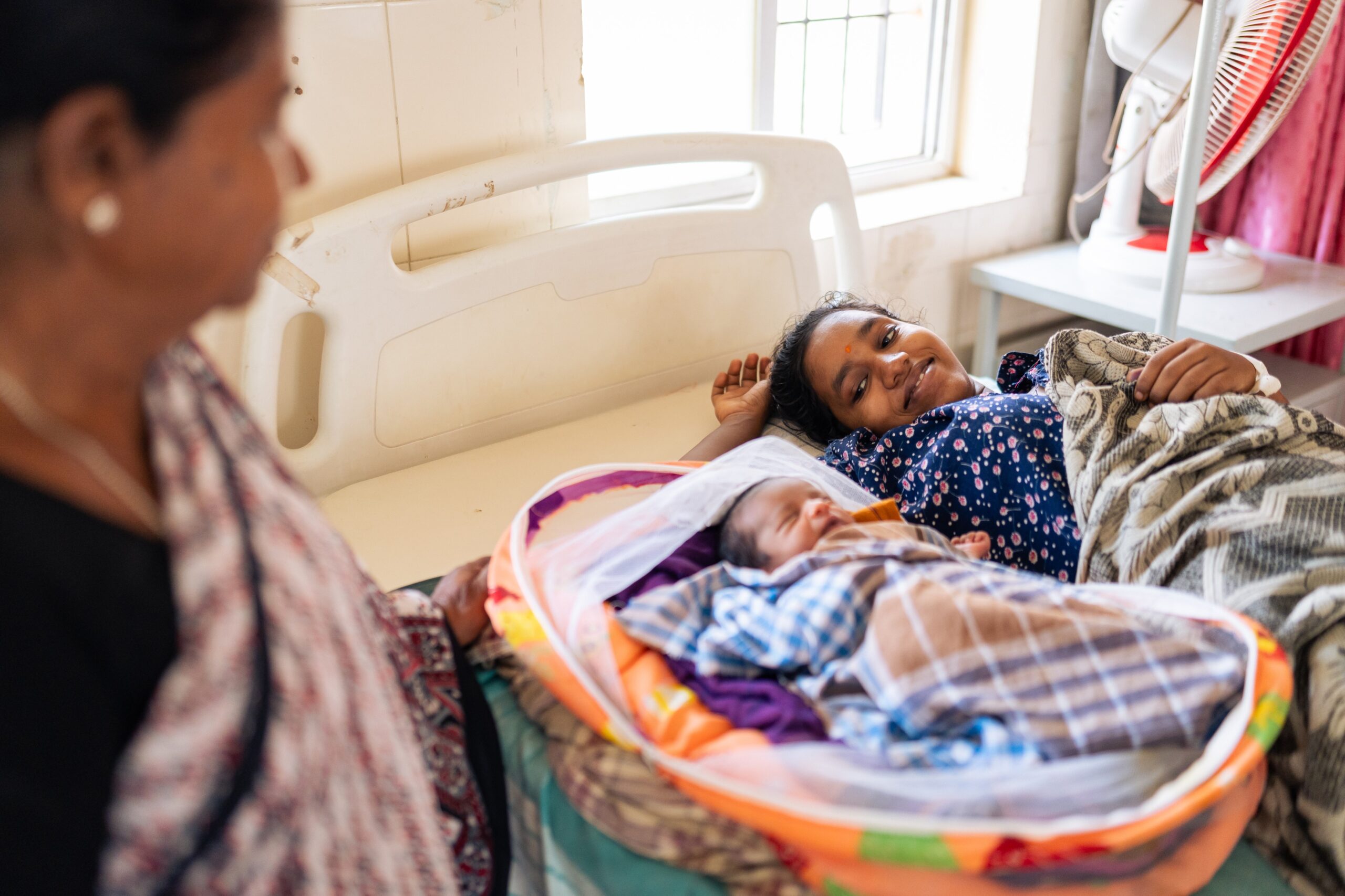 A smiling new mother looks at her baby at a hospital in Karnataka, India.